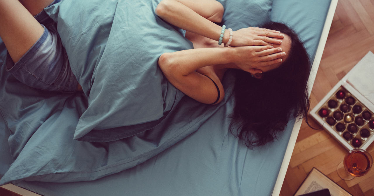 A woman holds her hands over her face in pain while laying in bed