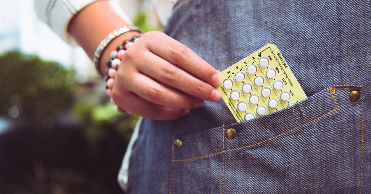 A woman's hand pulls a packet of birth control pills out of her pocket