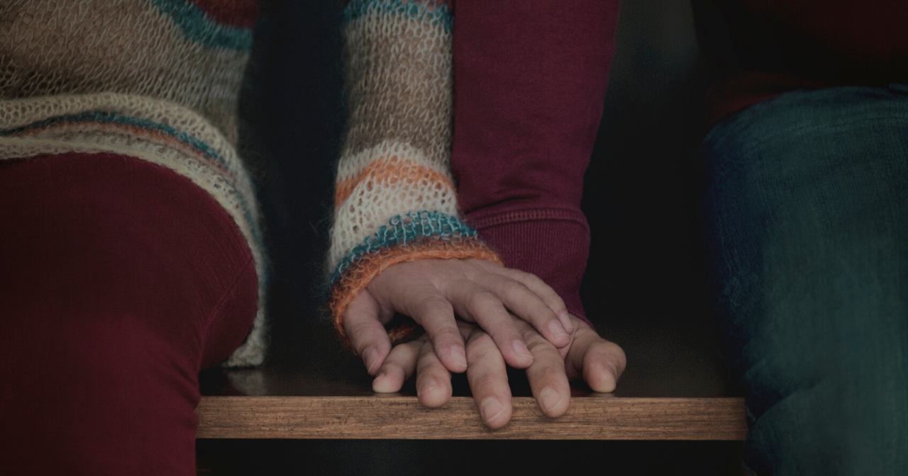 A woman's hand rests on top of her partner's on a bench.