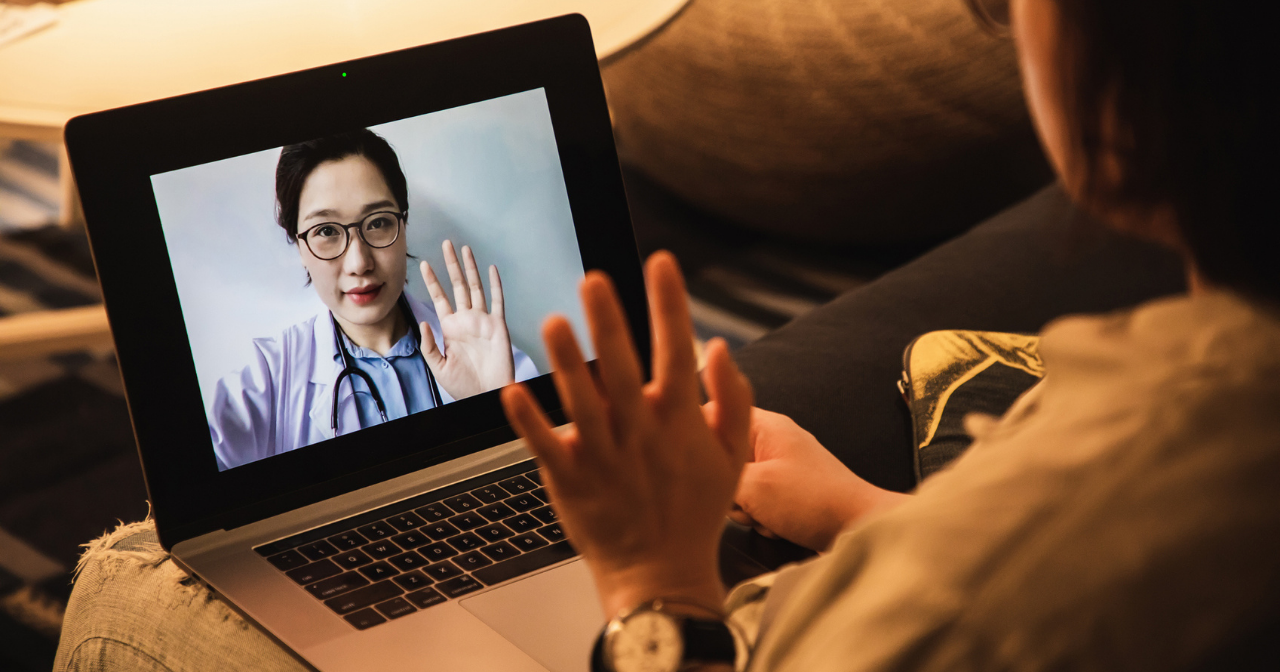 A provider waves at a patient through a laptop screen. 