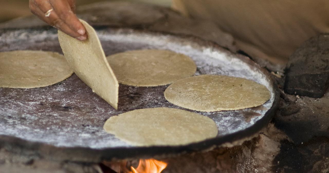 A hand flips a tortilla on a plate over a fire. 