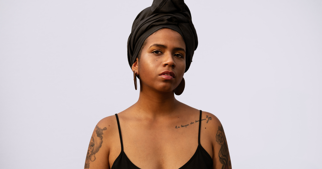 A Black woman looks directly into the camera, seriously. 