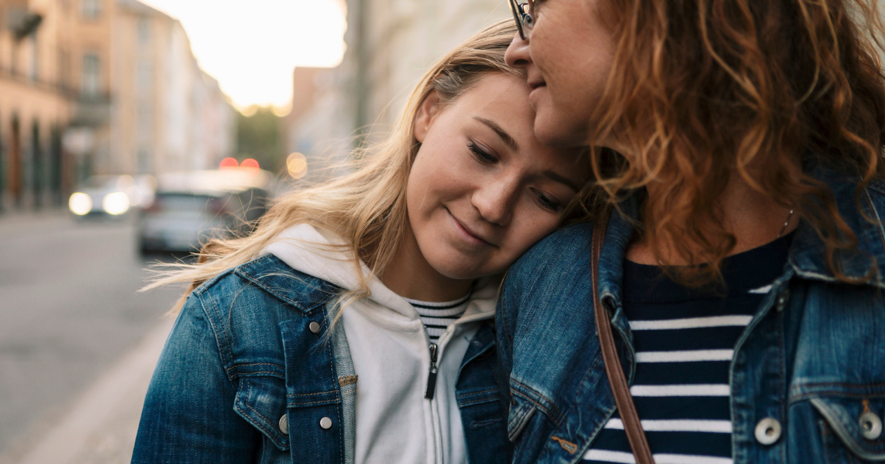 A mother and daughter hug casually on the street while they walk. 