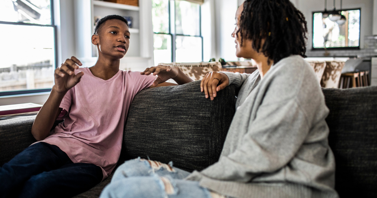 A mother and son sit on the sofa and have a conversation. 