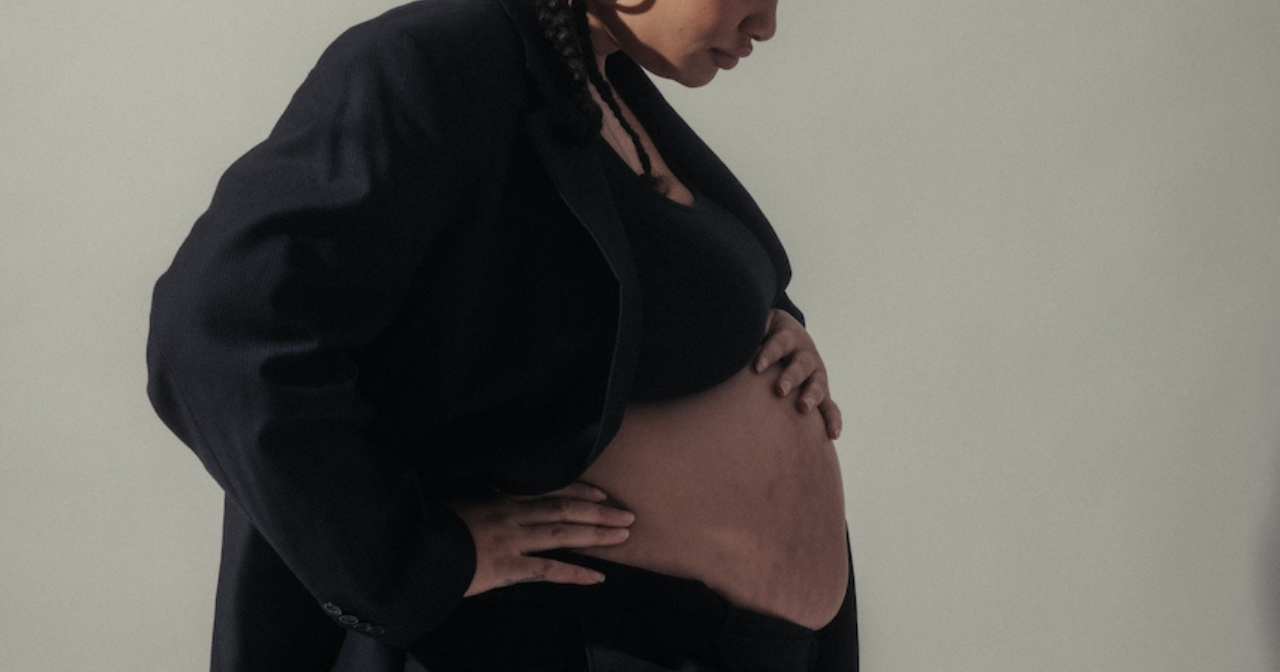 A close up photo of a Black, pregnant woman studying her belly.