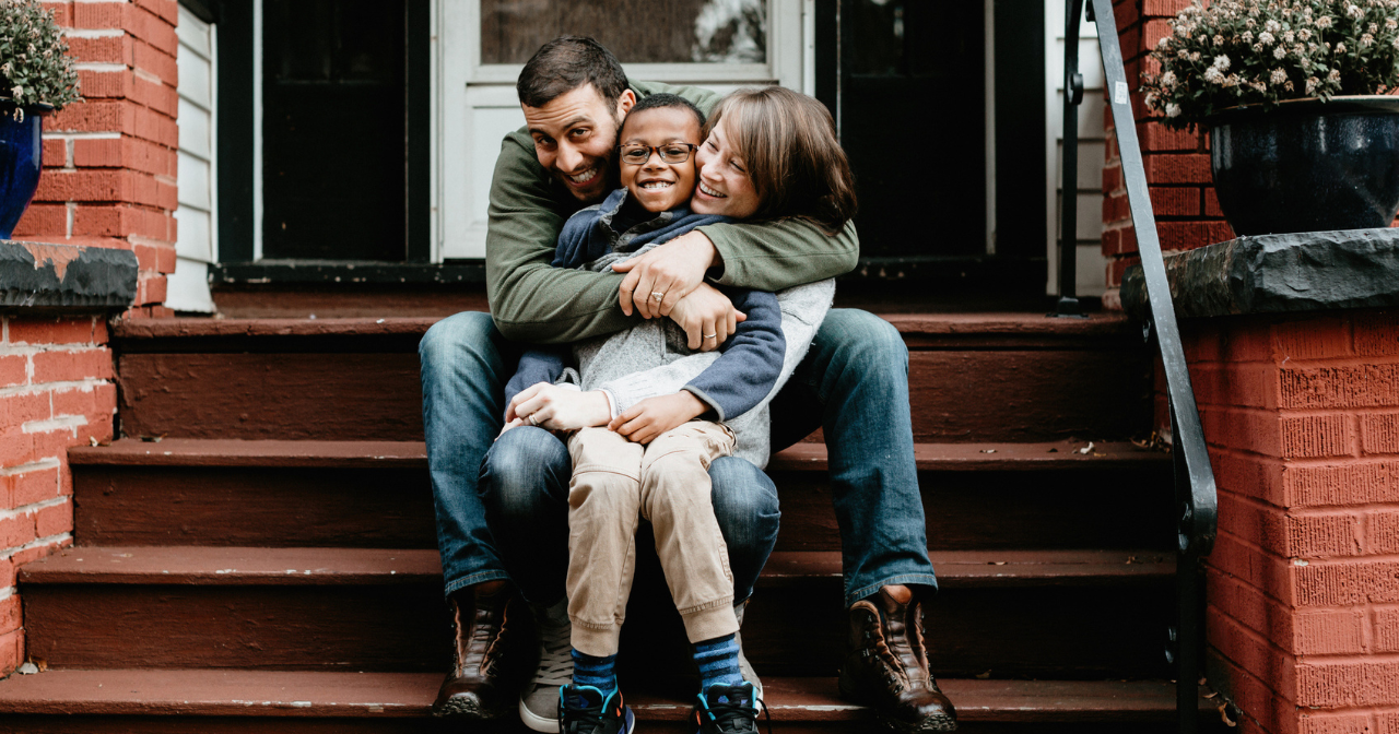 A happy family laughs and smiles sitting on the front stairs of their house.