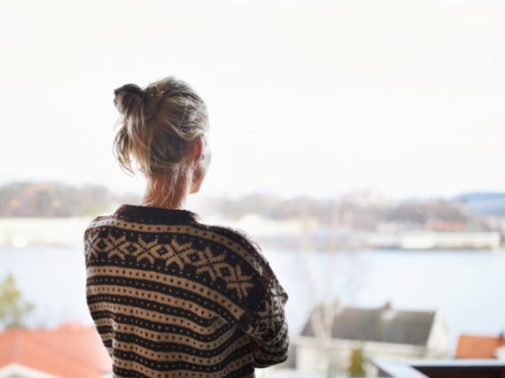 A woman with her back to the camera looks out a window 