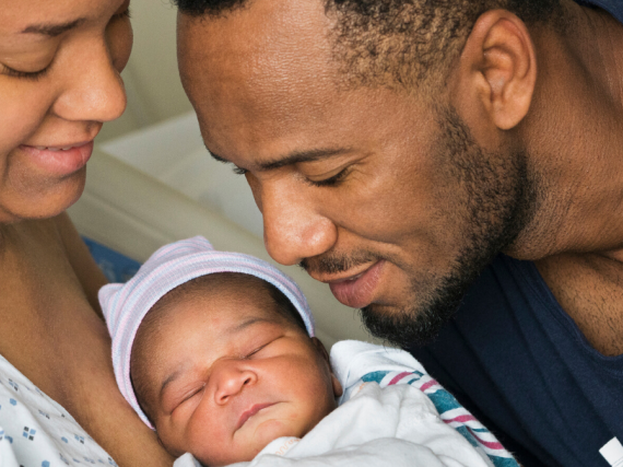 A black mother and father look at their newborn child.