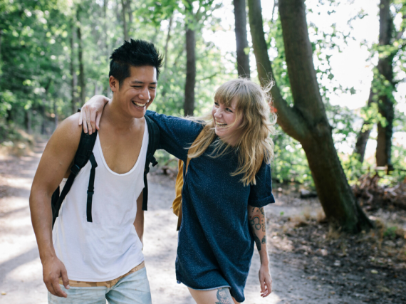A couple slings their arms over one another's shoulders while hiking. 