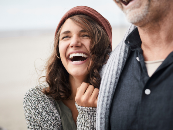 A dad and daughter hug and laugh on a beach. 
