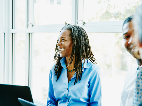 A Black woman laughs in a meeting with her laptop open in front of her. 