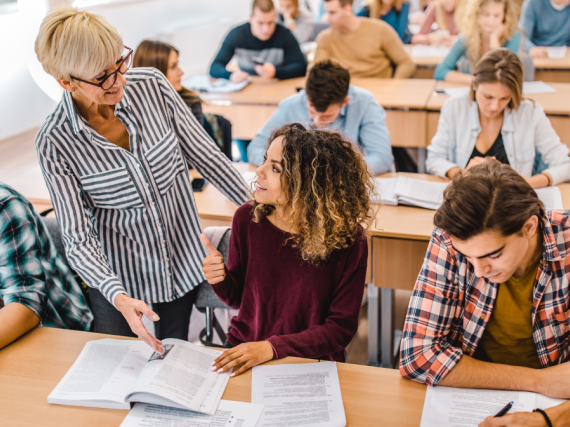 A teacher talks encouragingly to a student in a full classroom. 