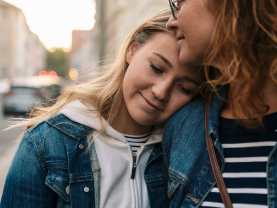 A mother and daughter hug casually on the street while they walk. 