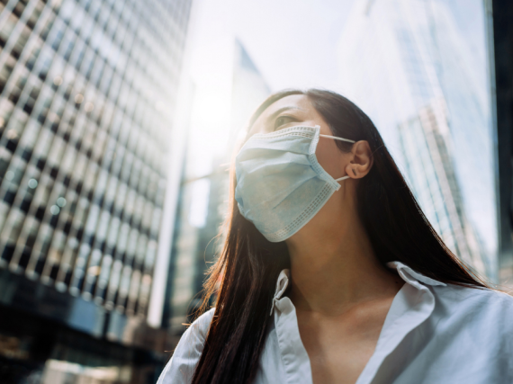 An Asian woman in a mask walks down a city street in business clothes. 