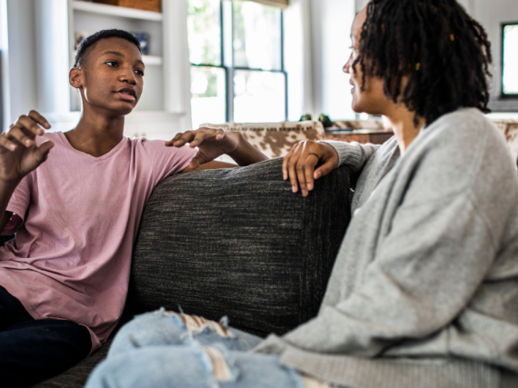 A mother and son sit on the sofa and have a conversation. 