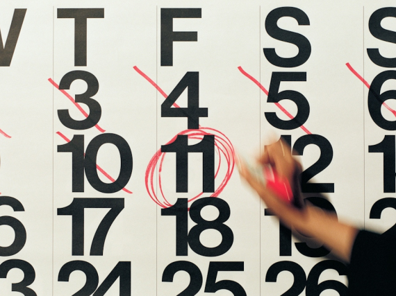 A hand holding a red marker is circling a date on a calendar. 