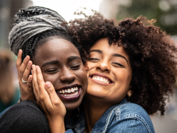 Two women hug very closely with large smiles