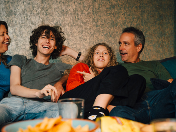 A family of four laugh on the sofa while watching TV. 